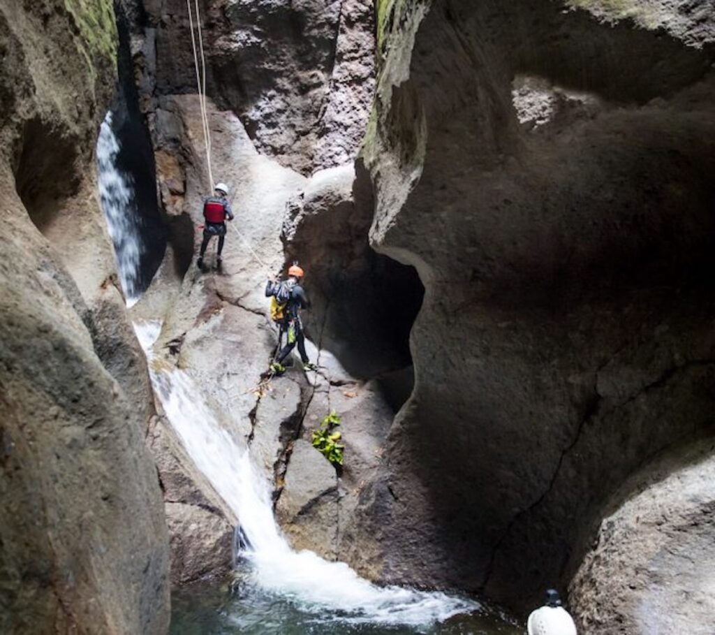 Guided canyoning descent in Dominica, rappelling down a rainforest waterfall into an emerald pool